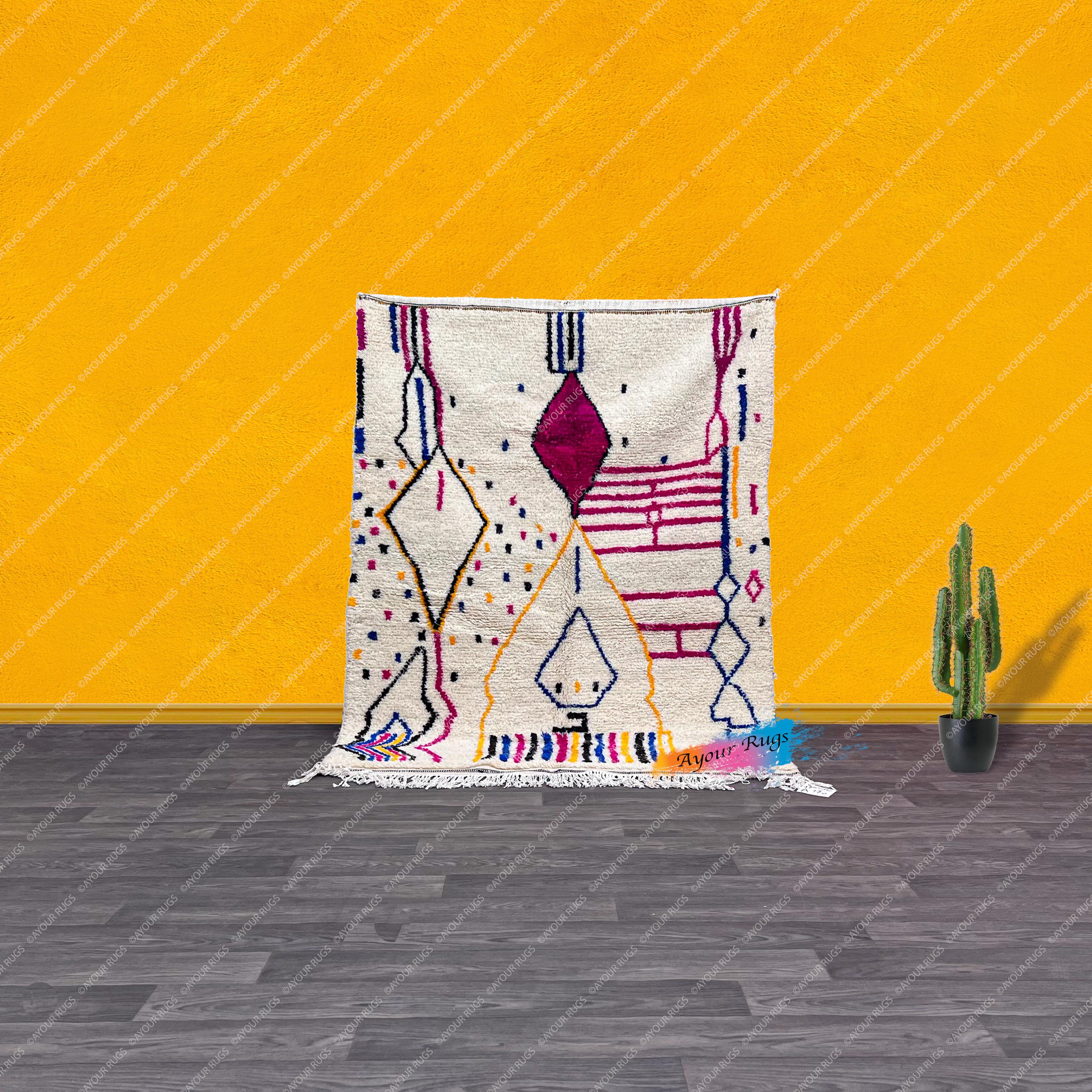 a vibrant, colorful rug with geometric patterns and designs, placed on a wooden floor against a bright yellow wall. Next to the rug, there is a small potted cactus plant, adding a touch of greenery to the scene.