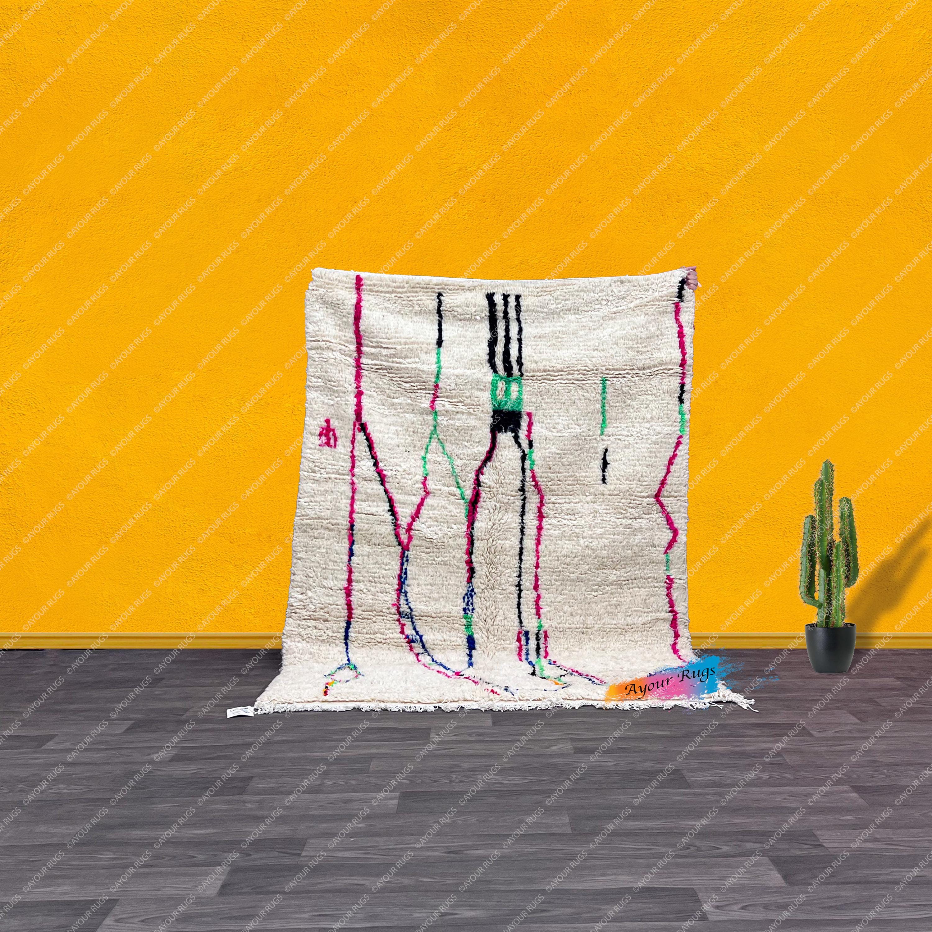 a vibrant rug with a colorful abstract design, placed on a wooden floor against a bright yellow wall. Next to the rug, there is a potted cactus plant, adding a touch of greenery to the scene.
