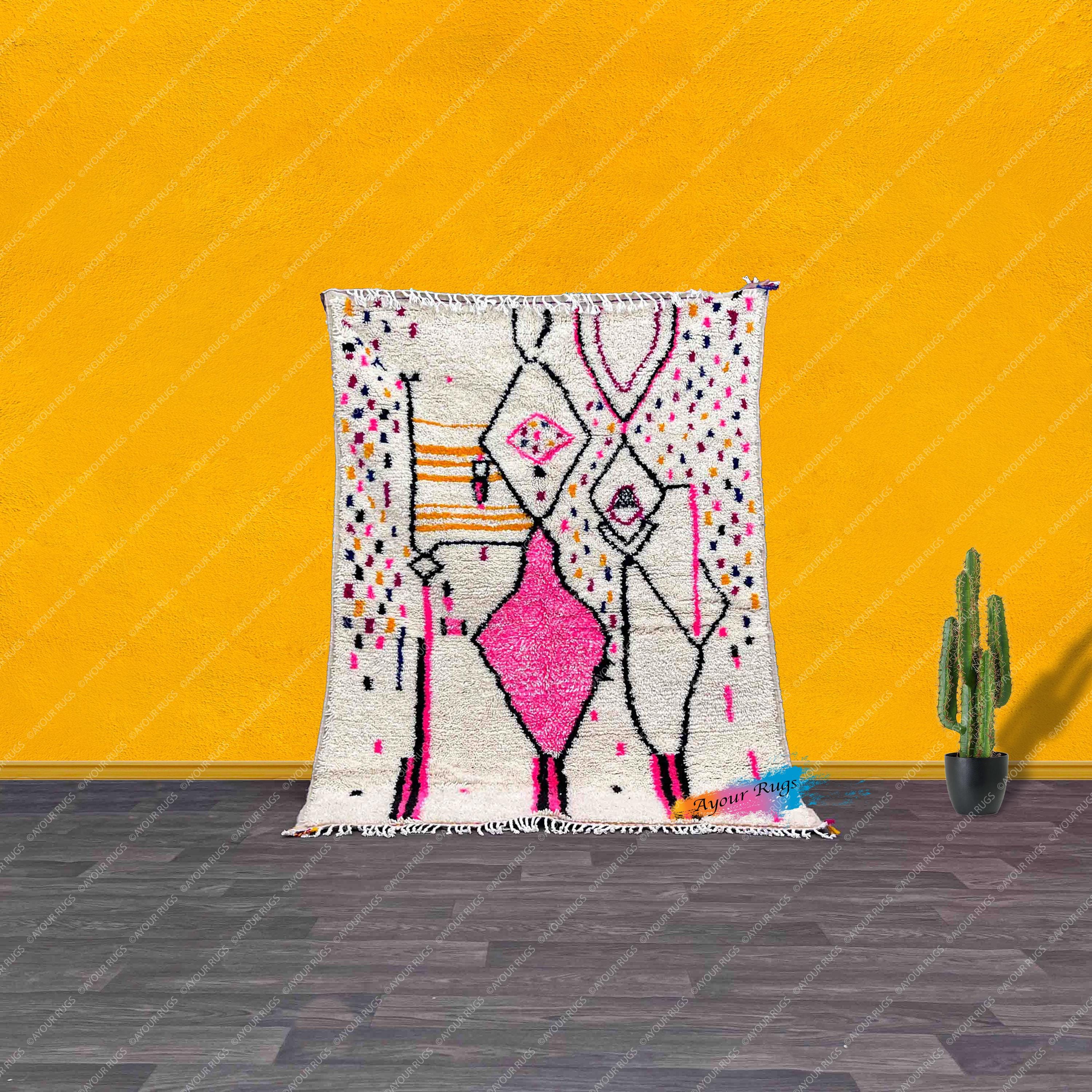 a vibrant, colorful rug with a geometric pattern, placed on a wooden floor against a bright yellow wall. Next to the rug, there is a potted cactus plant, adding a touch of greenery to the scene.