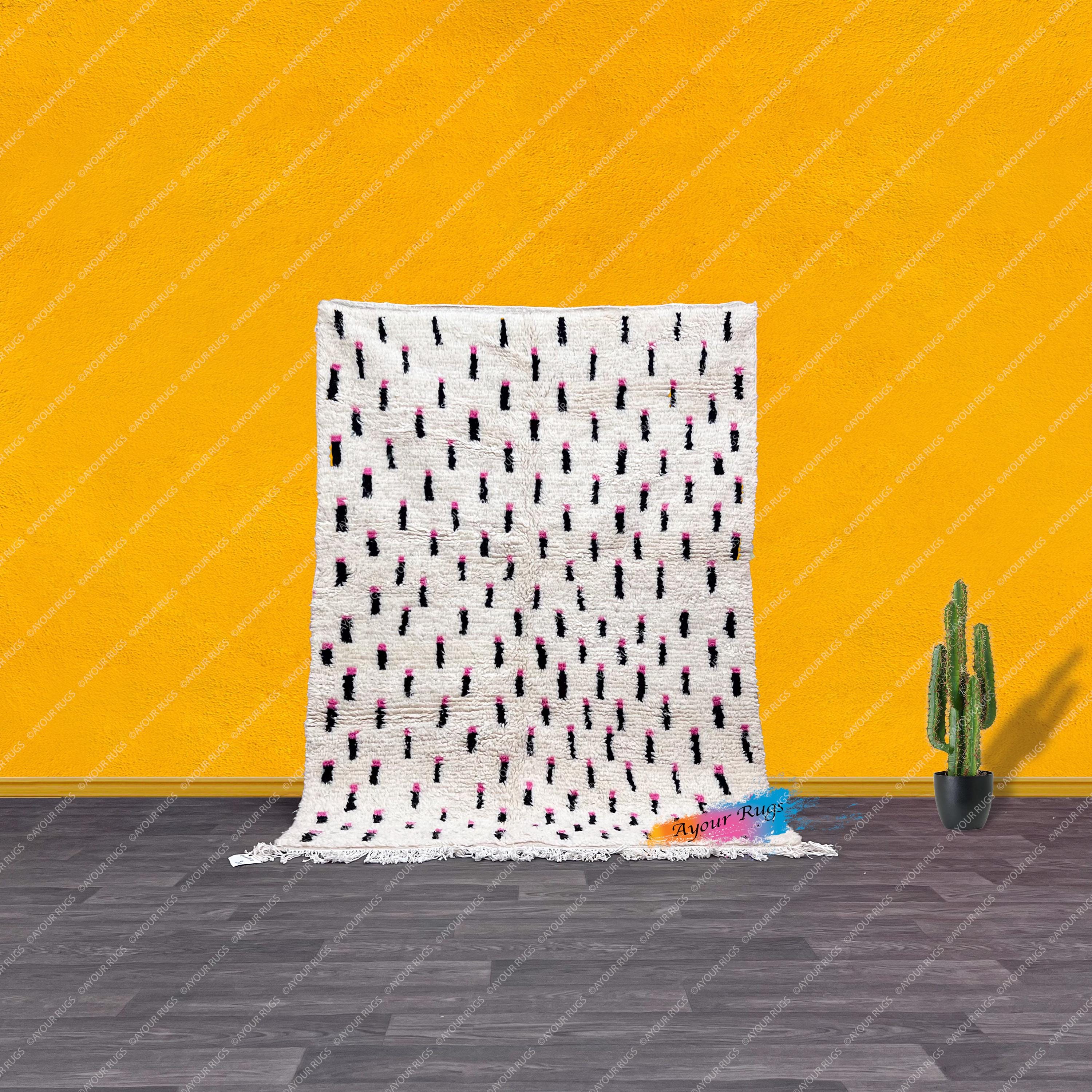 a white and black patterned rug with pink and black dots, placed on a gray floor against a bright yellow wall. Next to the rug is a potted cactus plant.